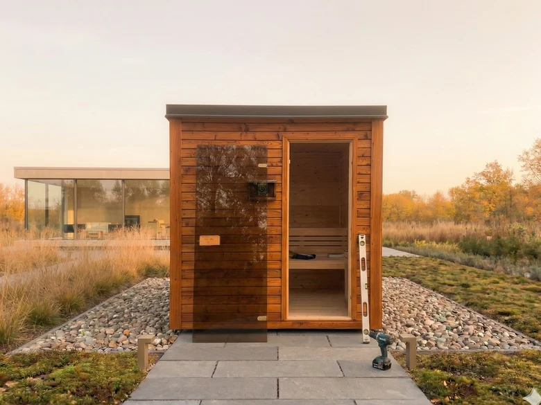 Nově postavená dřevěná sauna na kamenné cestě s nářadím.