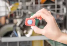 Ruka drží čisticí tabletu do myčky před otevřenou pračkou.