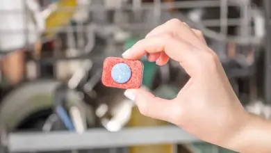 Ruka drží čisticí tabletu do myčky před otevřenou pračkou.
