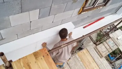 Muž montuje izolační desku na fasádu domu.