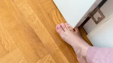Holá stopa na dřevěné podlaze u bílého nábytku.