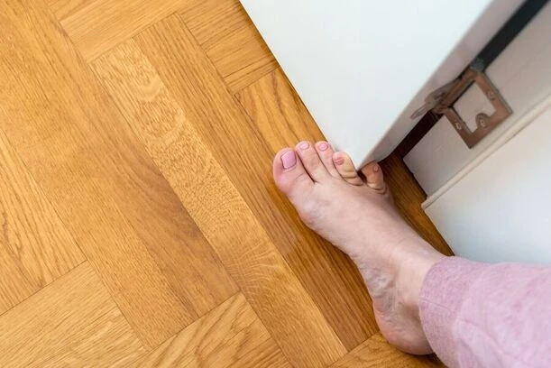 Holá stopa na dřevěné podlaze u bílého nábytku.
