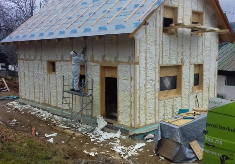 Stavebník aplikuje izolační pěnu na dřevěný rám pro provzdušněnou fasádu.