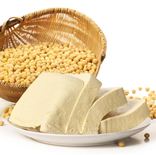 Kusky tofu před košem plným žlutých sójových bobů na bílém pozadí.