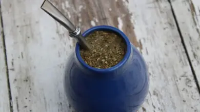 Modrá hrnek s yerbou maté a kovovou trubičkou na starém dřevěném stole.