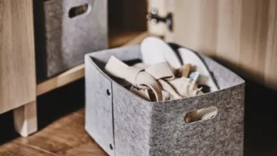 Šedý textilní úložný box s oblečením na dřevěné podlaze vedle skříně.