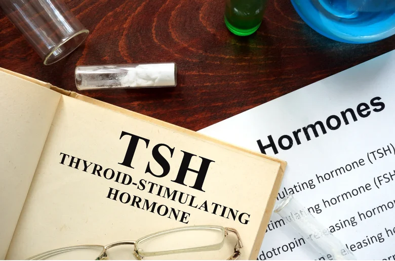 Otevřená kniha s textem o hormonu TSH na dřevěném stole.