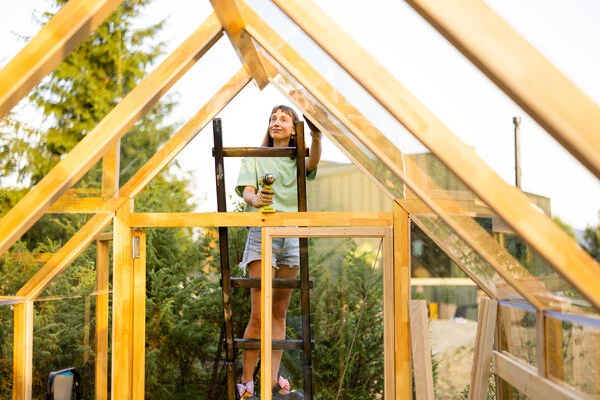 Dívka staví dřevěný rám skleníku na balkóně s nástrojem.