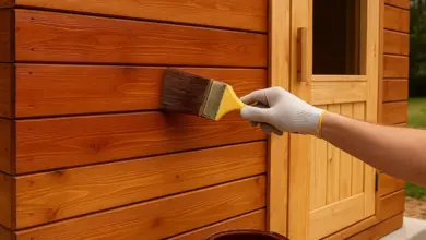 Ruka natíruje dřevěnou zeď sauny štětcem.