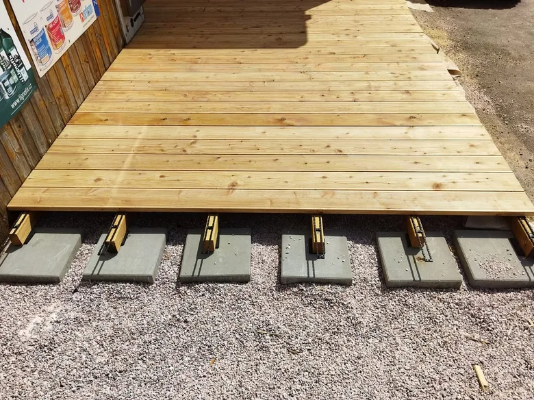 Nová dřevěná terasa postavená na betonových blokách vedle zdi.