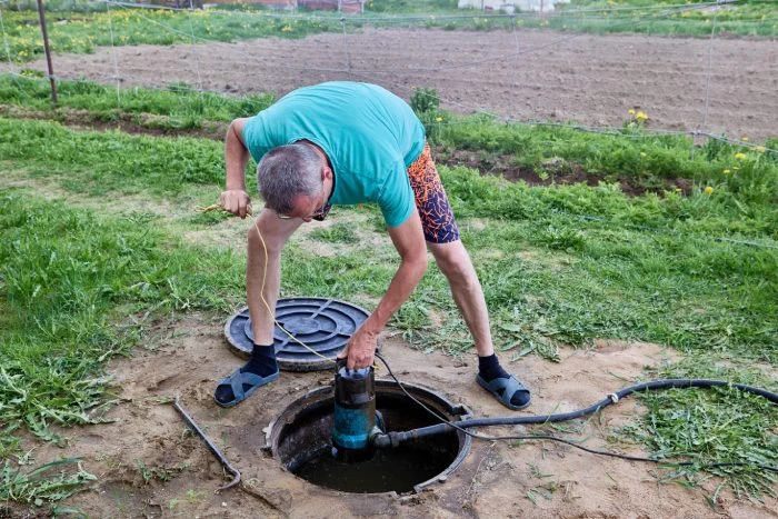 Muž instaluje čerpadlo do studny v zahradě.