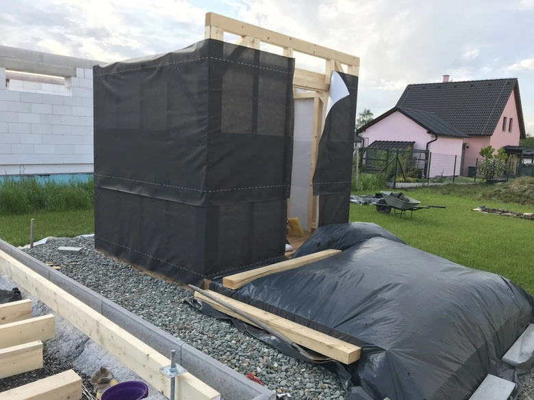 Sauna v stavbě s černou plachtou na štěrkovém podkladu