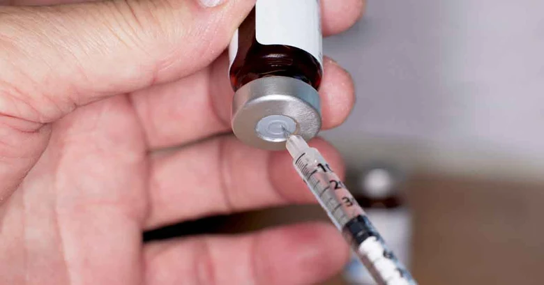 Ruka s ampulkou testosteronu a stříkačkou pro substituční léčbu.