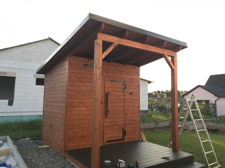 Nově postavená dřevěná sauna s přístřeškem na zahradě.