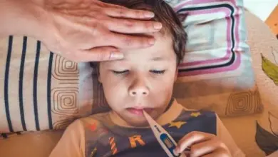 Dítě s teploměrem a rukou na čele při náhlé horečce