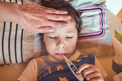 Dítě s teploměrem a rukou na čele při náhlé horečce