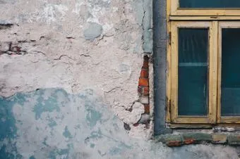 Zvětralá fasáda domu s oknem pro ilustraci bydlení.