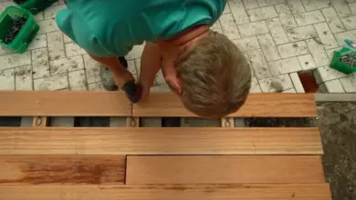 Muž montuje dřevěné prkna na kovové trámy pro terasu.
