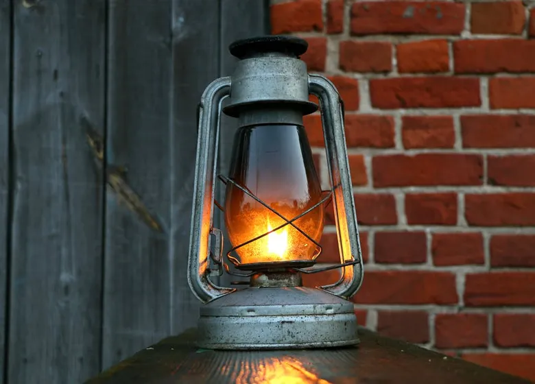 Zapálený olejový lampion na dřevěném povrchu před cihlovou zdí.